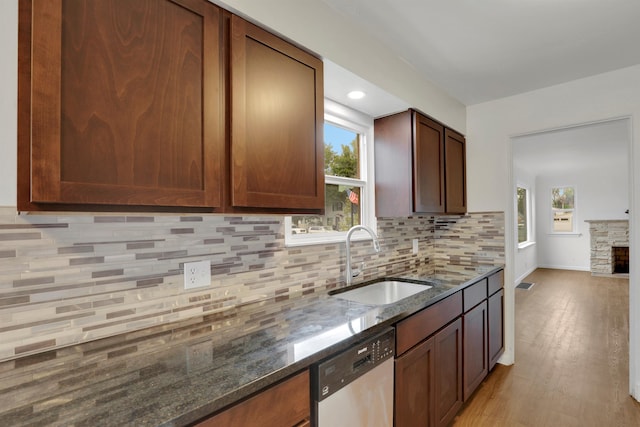 kitchen featuring backsplash, a sink, a stone fireplace, dark stone countertops, and dishwasher