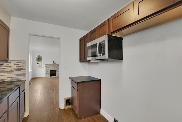 kitchen with a stone fireplace, stainless steel microwave, wood finished floors, and visible vents