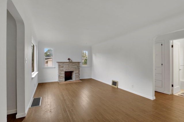 unfurnished living room featuring arched walkways, visible vents, a fireplace, and wood finished floors