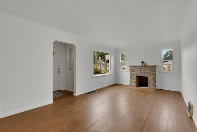 unfurnished living room with baseboards, visible vents, arched walkways, wood finished floors, and a stone fireplace