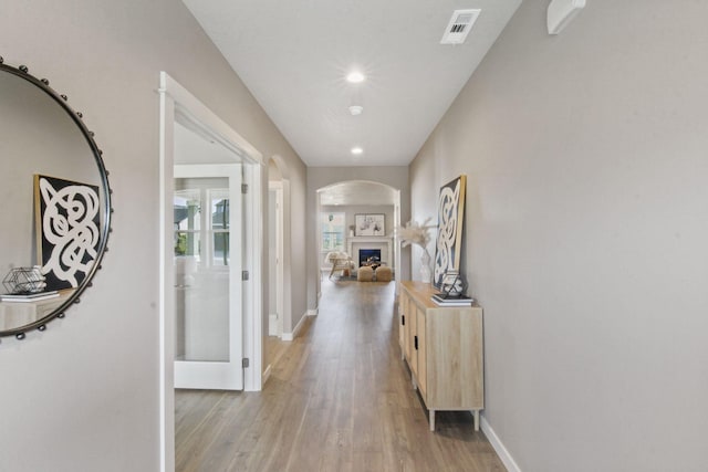 hallway with baseboards, visible vents, arched walkways, light wood-style floors, and recessed lighting