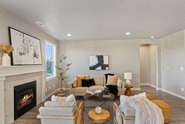 living room with arched walkways, a fireplace, wood finished floors, and visible vents