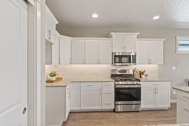 kitchen featuring stainless steel appliances, light wood-type flooring, white cabinets, and decorative backsplash