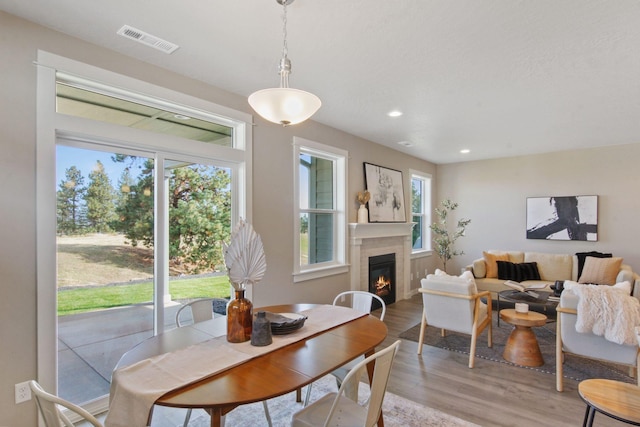 dining space featuring light wood-style flooring, a glass covered fireplace, visible vents, and recessed lighting