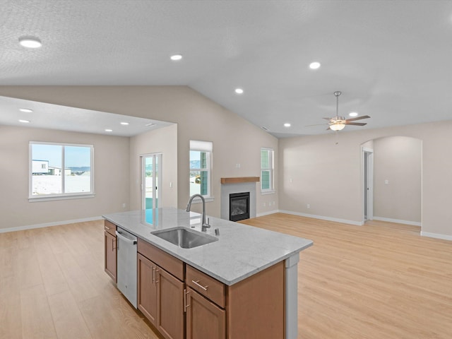 kitchen featuring a center island with sink, a glass covered fireplace, open floor plan, a sink, and dishwasher