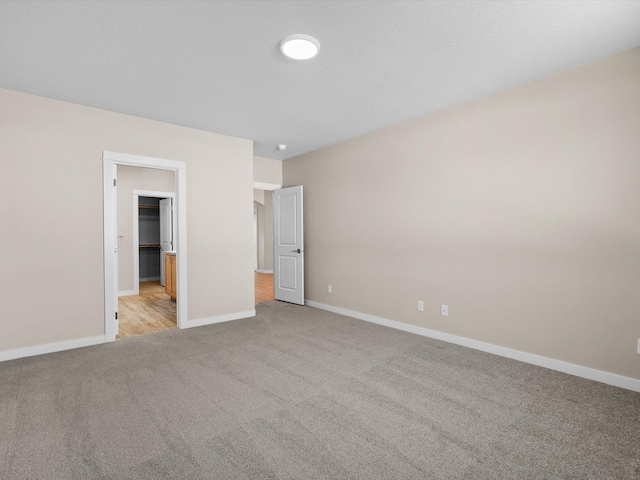 unfurnished bedroom featuring a walk in closet, light colored carpet, and baseboards