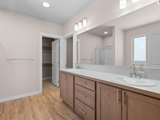 bathroom featuring double vanity, a sink, a shower stall, and wood finished floors