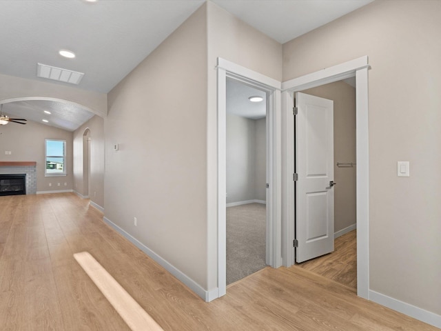 corridor with visible vents, arched walkways, baseboards, light wood-style flooring, and vaulted ceiling