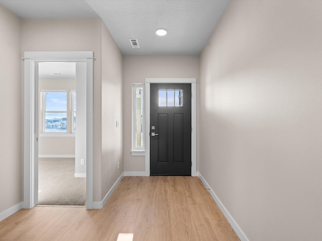 entryway with light wood finished floors, visible vents, and baseboards