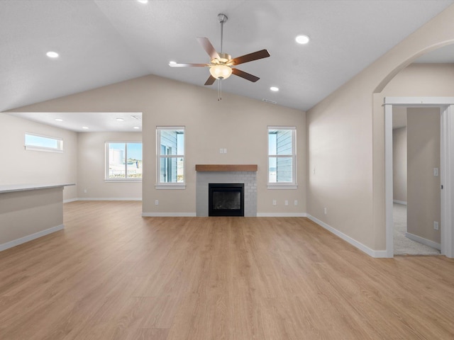 unfurnished living room with baseboards, lofted ceiling, light wood-style flooring, ceiling fan, and a fireplace