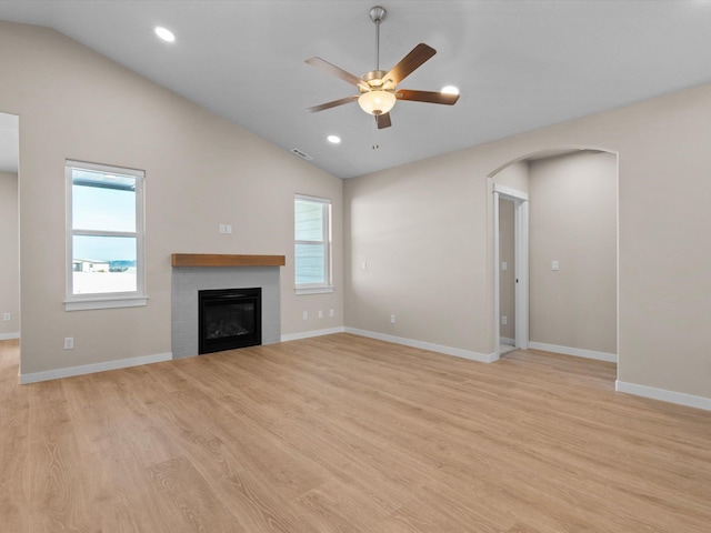 unfurnished living room featuring lofted ceiling, a glass covered fireplace, plenty of natural light, and light wood finished floors