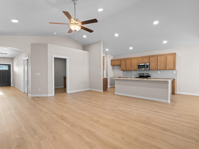 kitchen with arched walkways, light wood-style flooring, stainless steel appliances, light countertops, and a center island with sink