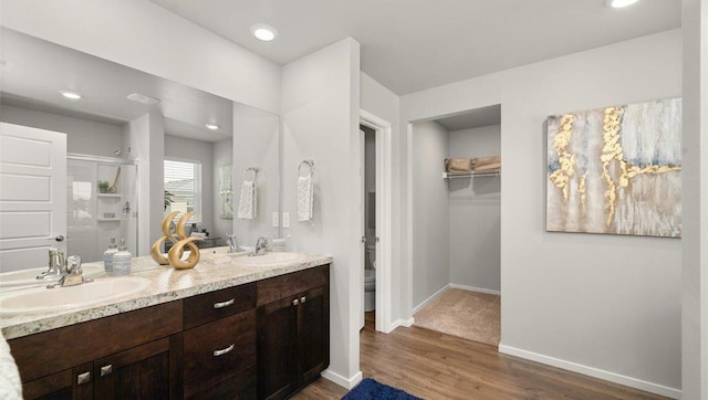 full bath featuring a stall shower, a sink, baseboards, and wood finished floors