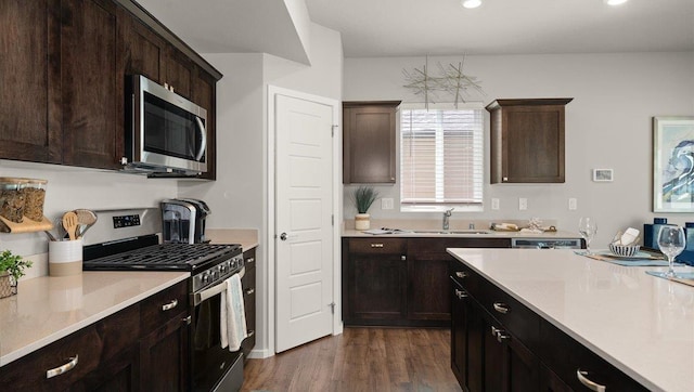 kitchen featuring dark brown cabinetry, stainless steel appliances, dark wood-type flooring, a sink, and light countertops