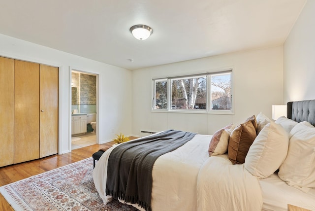 bedroom featuring a baseboard radiator, connected bathroom, and light wood finished floors