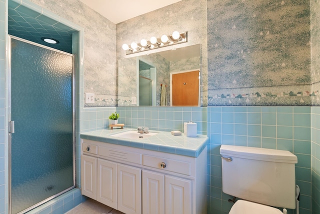 bathroom with tile walls, toilet, a stall shower, vanity, and wallpapered walls