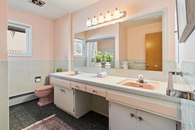 full bathroom with double vanity, toilet, baseboard heating, wainscoting, and a sink