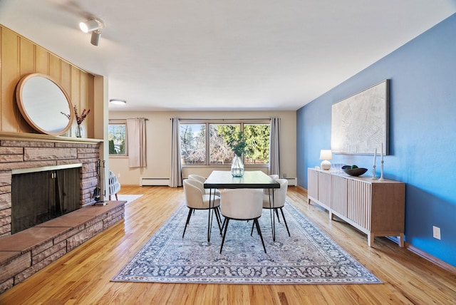 dining area featuring a fireplace with raised hearth, baseboard heating, wood finished floors, and a wealth of natural light