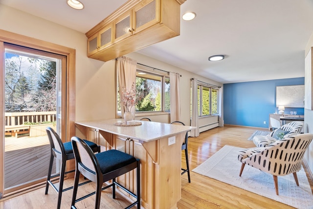 kitchen featuring baseboards, light wood-style flooring, glass insert cabinets, a breakfast bar area, and a baseboard heating unit