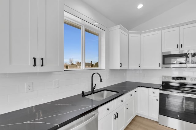 kitchen with tasteful backsplash, lofted ceiling, appliances with stainless steel finishes, white cabinets, and a sink