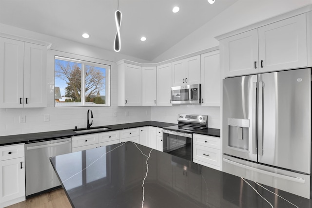 kitchen with lofted ceiling, appliances with stainless steel finishes, dark countertops, and a sink