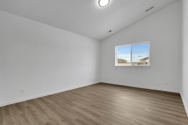 unfurnished room featuring visible vents, vaulted ceiling, baseboards, and wood finished floors