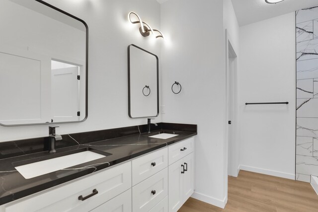 bathroom featuring double vanity, wood finished floors, a sink, and baseboards