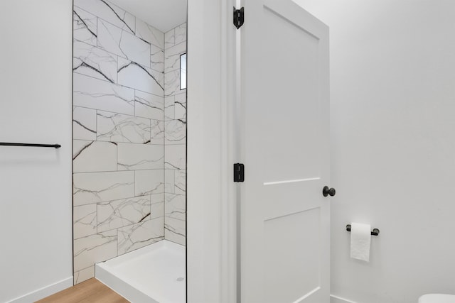 full bathroom with tiled shower, wood finished floors, and baseboards