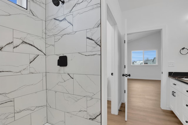 bathroom with vaulted ceiling, vanity, wood finished floors, tiled shower, and baseboards