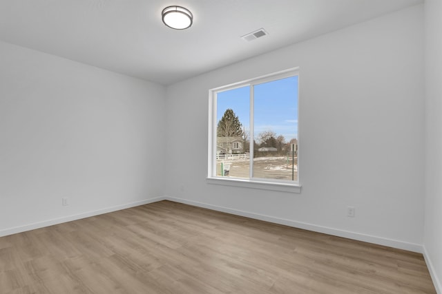 empty room with visible vents, light wood finished floors, and baseboards