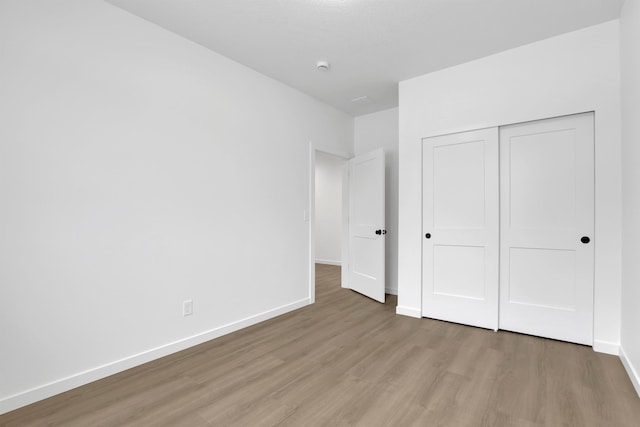 unfurnished bedroom featuring a closet, light wood-type flooring, and baseboards