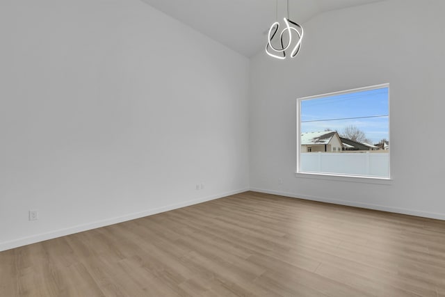 empty room with vaulted ceiling, a notable chandelier, wood finished floors, and baseboards