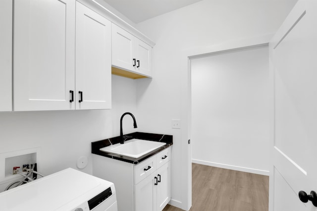 kitchen with dark countertops, light wood-style flooring, white cabinets, a sink, and washer / dryer