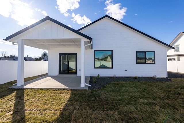 back of property featuring board and batten siding, a patio area, fence, and a lawn