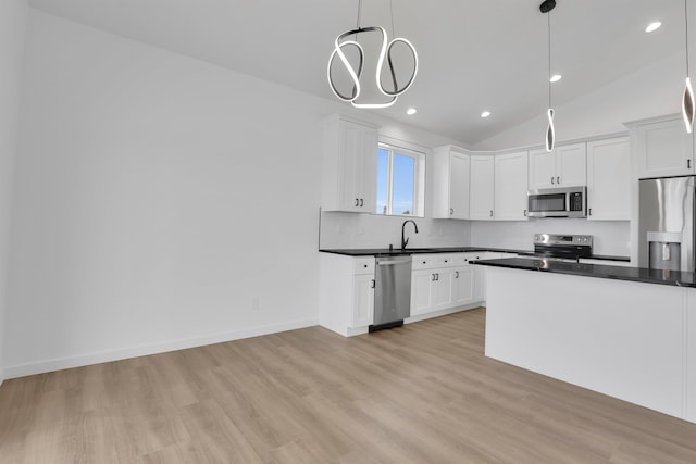 kitchen featuring light wood finished floors, decorative backsplash, dark countertops, appliances with stainless steel finishes, and a sink