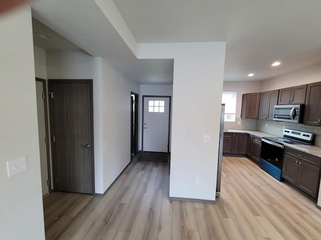 kitchen with light wood-type flooring, appliances with stainless steel finishes, decorative backsplash, and light countertops