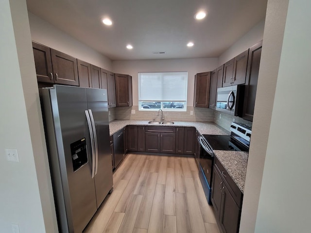 kitchen featuring light wood finished floors, stainless steel appliances, decorative backsplash, a sink, and light stone countertops