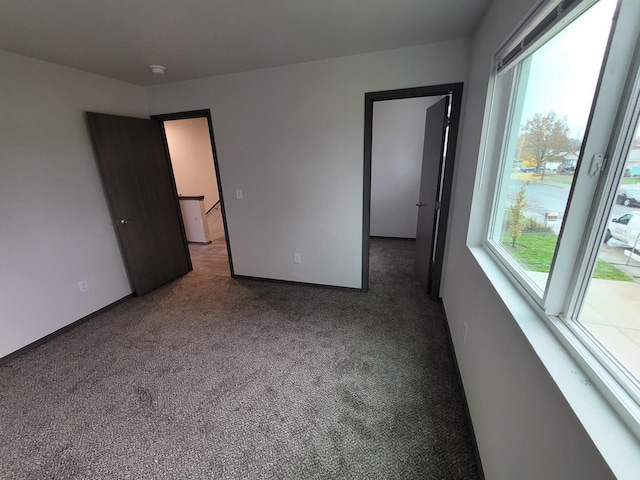 unfurnished bedroom featuring multiple windows, carpet flooring, and baseboards