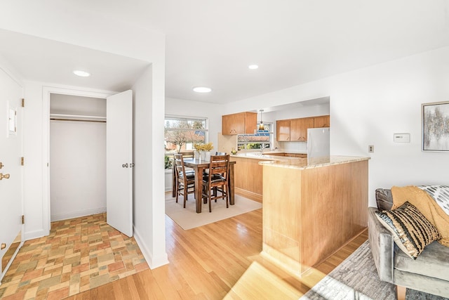 kitchen featuring light wood finished floors, brown cabinetry, freestanding refrigerator, a sink, and a peninsula