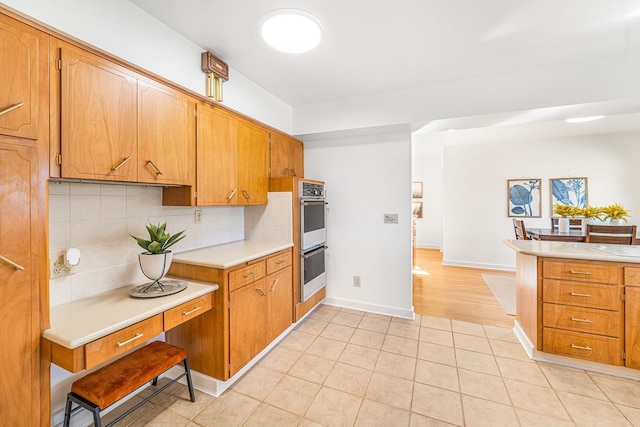 kitchen featuring light tile patterned floors, stainless steel double oven, baseboards, light countertops, and decorative backsplash