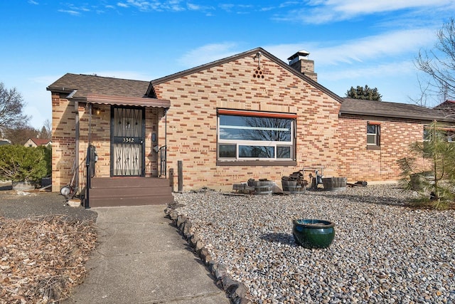 view of front of home with a shingled roof, a chimney, and brick siding