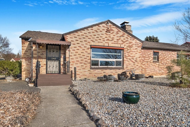 view of front of home with a shingled roof, brick siding, a chimney, and central AC unit