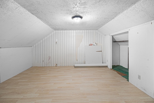 additional living space with vaulted ceiling, a textured ceiling, and wood finished floors