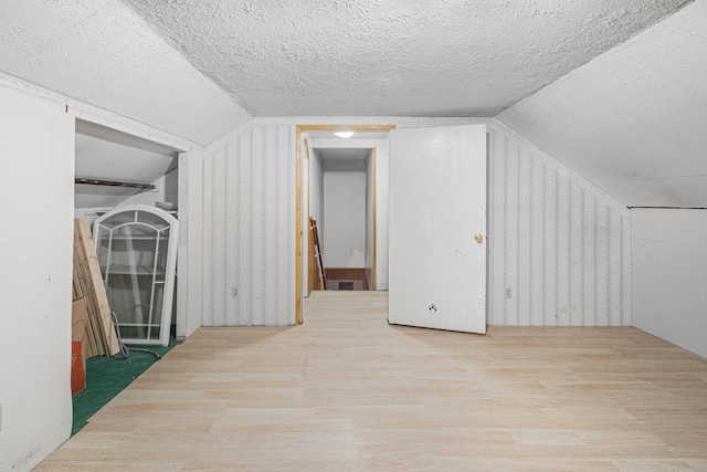 additional living space featuring vaulted ceiling, a textured ceiling, and wood finished floors