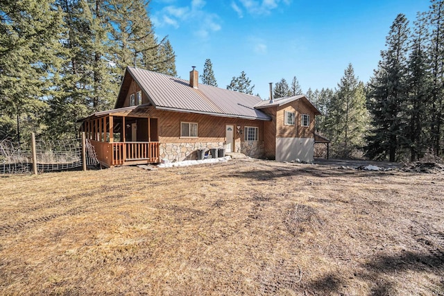 exterior space with central air condition unit, stone siding, a chimney, and metal roof