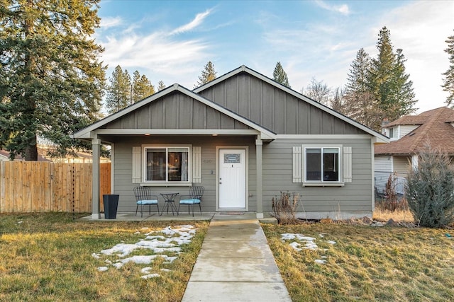 bungalow with a front lawn, board and batten siding, a patio area, and fence