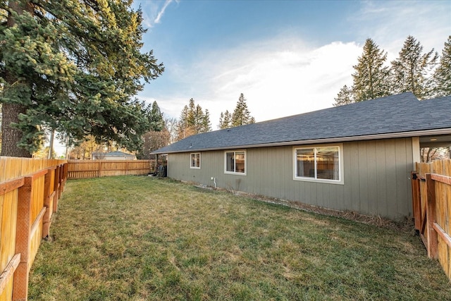 rear view of house featuring a fenced backyard, a lawn, and roof with shingles