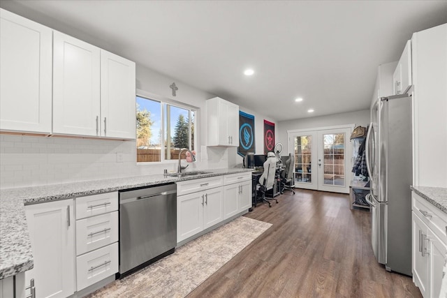 kitchen with wood finished floors, a sink, french doors, appliances with stainless steel finishes, and decorative backsplash