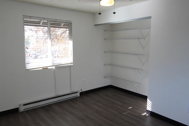 spare room featuring a baseboard radiator, baseboards, dark wood finished floors, and a textured ceiling