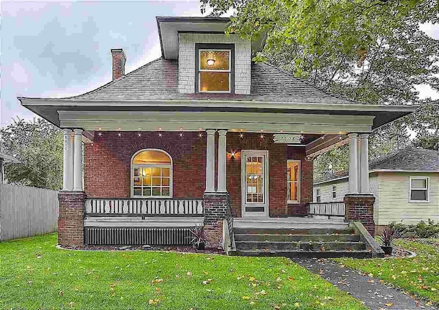 view of front facade with covered porch, brick siding, a chimney, and a front lawn